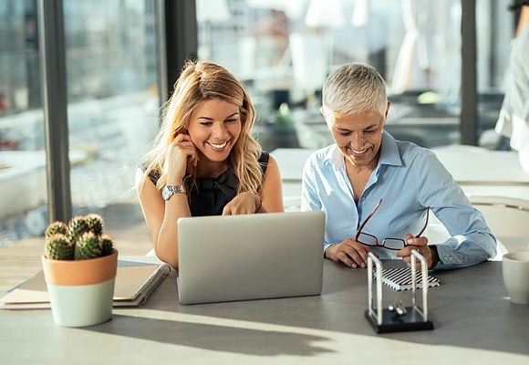 Eine junge und eine ältere Frau arbeiten gemeinsam am Schreibtisch vor dem Laptop©iStock/bernardbodo