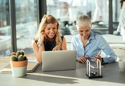 Eine junge und eine ältere Frau arbeiten gemeinsam am Schreibtisch vor dem Laptop©iStock/bernardbodo